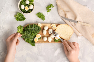 Woman eating fresh boiled quail eggs with greens and piece of bread on light background