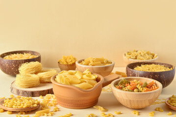 Bowls with different raw pasta on light background