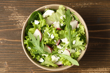 Bowl of healthy salad with radish on wooden background