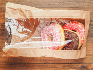 A pink donut with sprinkles on top is sitting in a paper bag. The donut is placed on a wooden...