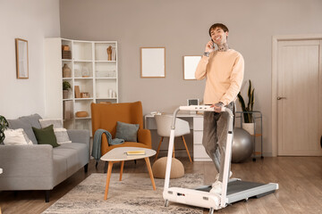 Young man talking by mobile phone on treadmill at home