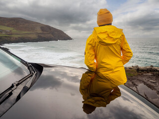 Woman standing black car and looking at stunning nature scenery of rough stone coastline and...