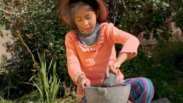 latina girl grinding in a mortar or batan in the backyard of her house in la paz, bolivia - cooking concept