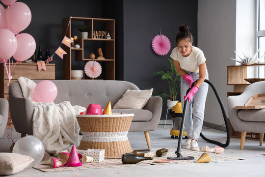 Young Asian woman using vacuum cleaner in messy room after Birthday party