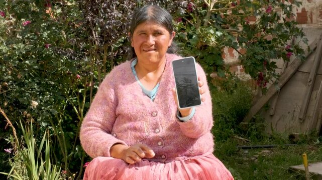 cholita adult woman in pollera showing her cell phone to the camera in the courtyard of her house in La Paz Bolivia - concept of older adults