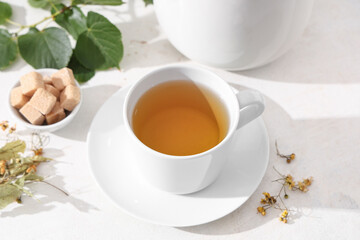 Cup of tasty linden tea with leaves on white background