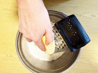 Hand grating cold butter into flour using metal grater for baking preparation in home kitchen. High quality photo