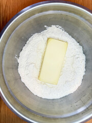 Block of butter placed on flour in a stainless steel mixing bowl, essential ingredients for baking preparation. High quality photo