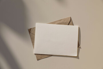 Blank horizontal greeting card, invitation mockup, craft envelope in sunlight on beige table...