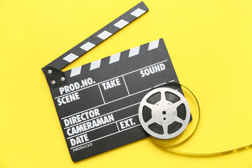 Movie clapper with film reel on yellow background