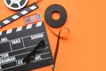 Movie clapper with film reels, cinema ticket and glasses on orange background