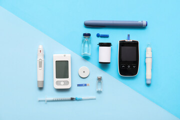 Modern glucometers with lancet pens, insulin ampules and syringe on color background