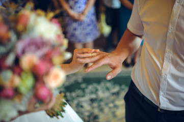 Close-up of a bride and groom exchanging wedding rings, with a beautiful bouquet in the bride's...