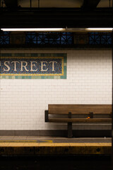 A bench is sitting in front of a white wall with a sign that says 