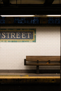 A bench is sitting in front of a white wall with a sign that says "Street". The bench is empty and the sign is in black lettering on a white background. Scene is calm and quiet, with the bench
