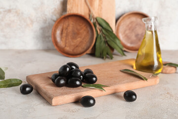 Wooden board with tasty black olives and leaves on light background