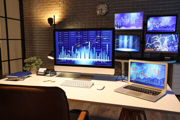 Naklejka premium Computer and laptop with stock data on trader's desk in dark office at night