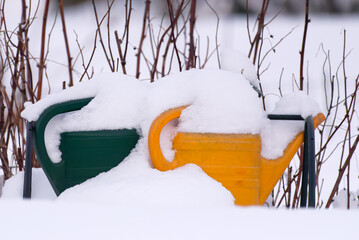 Green and yellow watering cans fully covered with deep snow in winter snowy scene.