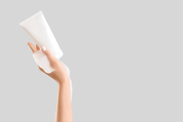 Female hand with bottle of cosmetic product and foam on grey background