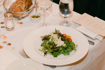 Elegant salad served on a white plate at a dining table in a restaurant during an evening gathering