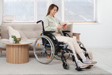 Young woman in wheelchair using mobile phone at home
