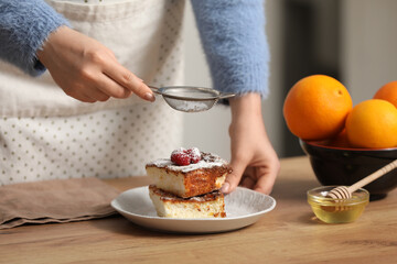 Woman decorating delicious cake with sugar powder in kitchen. Closeup