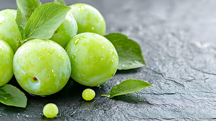 Obraz premium Fresh green plums on dark stone, water droplets, leaves. Food photography for recipe, website