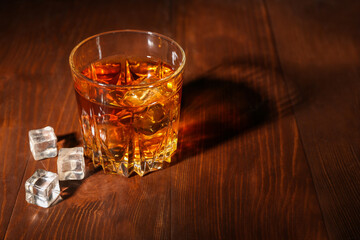 Glass of rum with ice cubes on wooden background