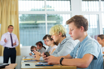 Group of focused teenagers using phones at class in auditorium