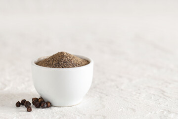 Bowl with black pepper powder and peppercorns on white background