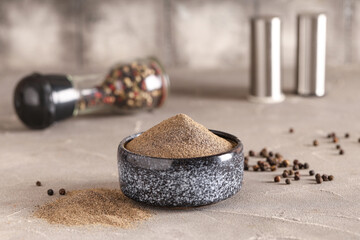 Bowl with black pepper powder and peppercorns on grey table