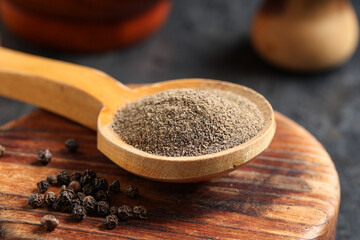Wooden spoon with black pepper powder and peppercorns on dark background, closeup