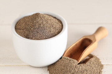 Bowl with black pepper powder on white wooden background
