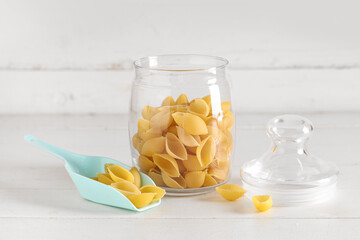 Scoop and jar with raw conchiglie pasta on white wooden background