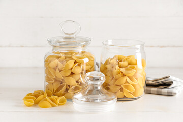 Jars with raw conchiglie pasta on white wooden background