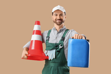 Male mechanic with canister and traffic cone on beige background