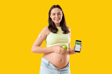 Young pregnant woman with glucose sensor and mobile phone on yellow background. Gestational...