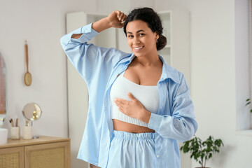Young African-American woman checking her breast in bathroom. Cancer awareness concept