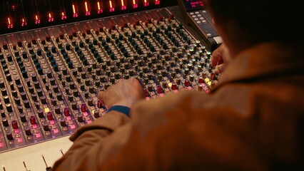 Audio technician producing new music at mixing console in control room, twisting knobs, pressing...