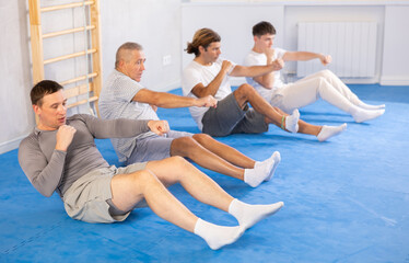 Group of men of different ages train abdominal muscles and do punches at the same time during karate or judo training