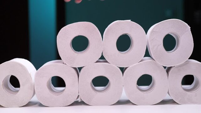 Hand placing toilet paper roll on a pyramid of toilet paper rolls