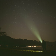 Person using headlamp at night, overlooking a lake with mountains and starry sky.  Perfect for travel, adventure, or exploration themes
