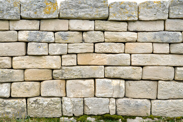 Fototapeta premium A close-up photo of a weathered stone wall with cracks and moss, showcasing earthy tones and rough textures.
