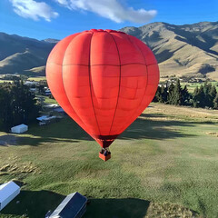 Obraz premium Red hot air balloon soaring over valley, scenic mountain background, adventure tourism