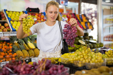 Portrait of beautiful russian young woman buying fresh grape at grocery shop