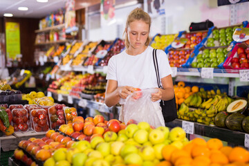 Fifteen-year-old girl who came to the store chooses ripe apples on the counter to buy them
