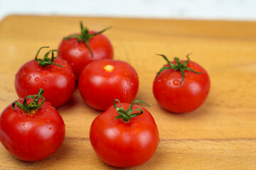 Fresh red tomatoes with water droplets on wooden cutting board