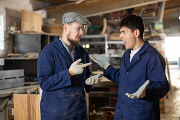 Young male carpenters quarrel during work process in wooden workshop