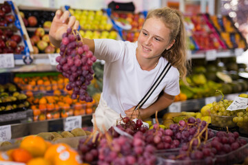 Young american girl choosing sweet grape at grocery section of supermarket