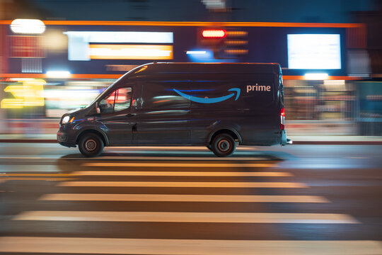 LOS ANGELES, CA - February 12, 2025: Amazon Prime delivery van rushing through city traffic, crossing illuminated street intersection at night in West Hollywood, California.